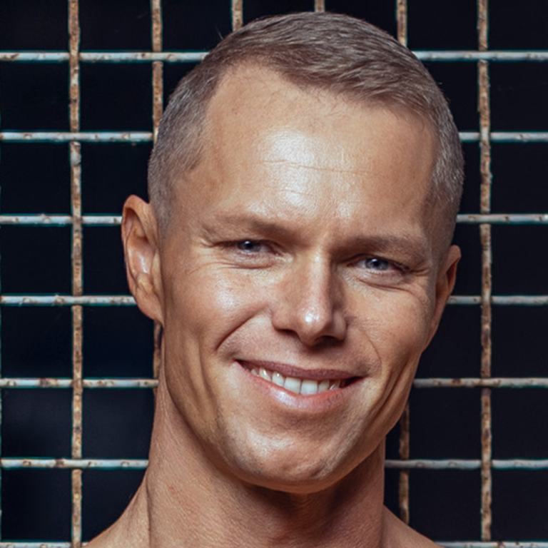 Lächelnder Mann mit kurzem Haar vor einem Gitterhintergrund.